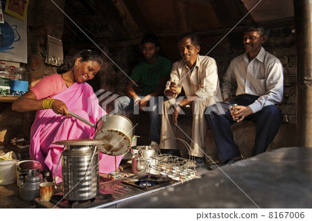 Indian female vendor pouring chai in cup with customers sitting at stall 8167006