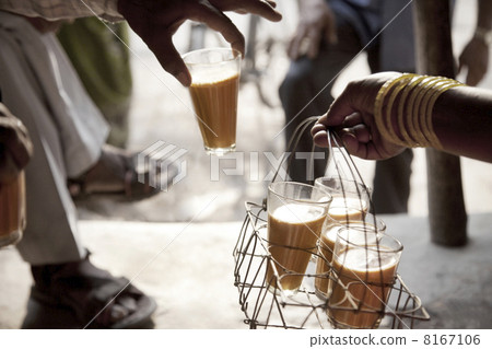 Male hand taking a glass of chai from tray held by woman 8167106