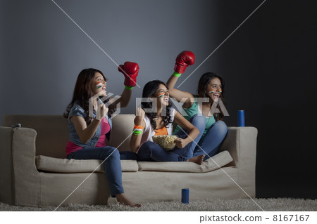 Cheerful young female friends watching boxing match together at home Cheerful young female friends watching boxing match together at home 8167167