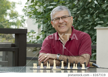 Portrait of senior man smiling while sitting by table with chess board 8167319