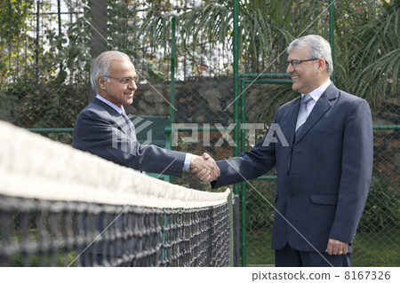 Senior male business executives shaking hands while standing in a tennis court 8167326
