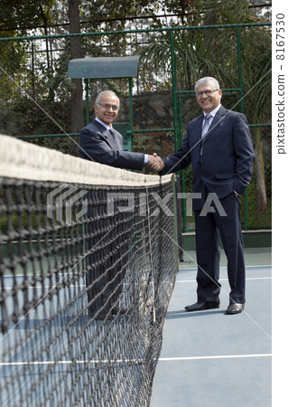 Portrait of senior professionals shaking hands over a tennis net in court 8167530