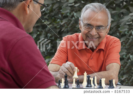 Senior man smiling at friend while holding chess piece 8167533
