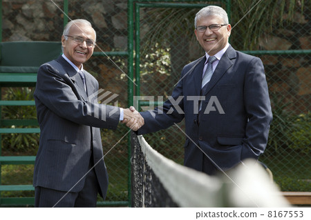 Portrait of happy senior male professionals shaking hands over tennis net in court 8167553