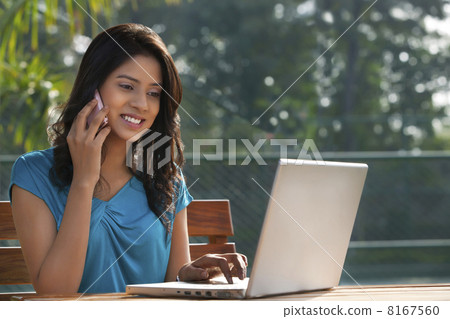 Young woman answering phone call while working on laptop 8167560