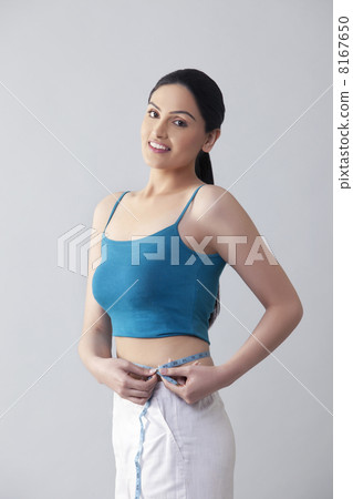 Portrait of young woman measuring waist isolated over gray background 8167650