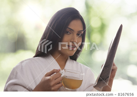 Portrait of young woman holding newspaper while drinking tea Portrait of young woman holding newspaper while drinking tea 8167656