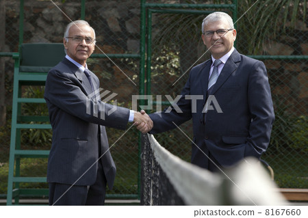 Portrait of senior male professionals shaking hands over tennis net in court Portrait of senior male professionals shaking hands over tennis net in court 8167660