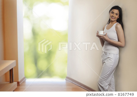 Portrait of beautiful young woman leaning on wall while holding cup of coffee 8167749