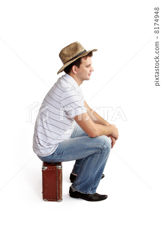 young man in a hat sitting on a suitcase 8174948