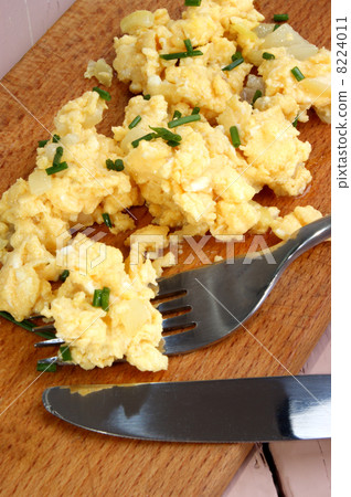 Scrambled eggs with chives, knife and fork on a wooden board 8224011