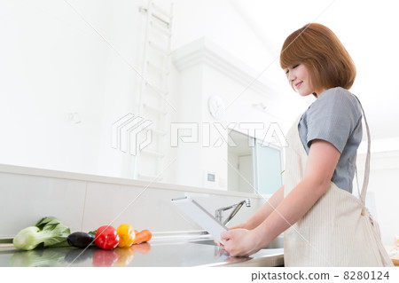 A woman cooking while watching a tablet 8280124