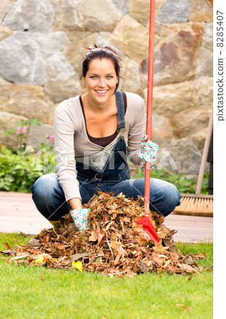 Cheerful woman sweeping leaves autumn pile backyard Cheerful woman sweeping leaves autumn pile backyard 8285407