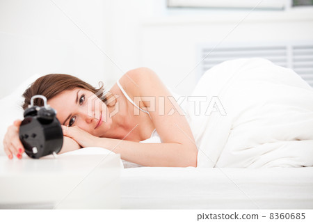 woman lying in bed with alarm clock. woman lying in bed with alarm clock. 8360685