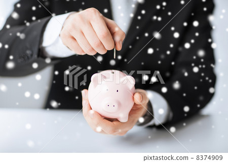 man putting coin into small piggy bank 8374909