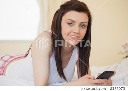 Smiling girl looking at camera using a mobile phone lying on a b Smiling girl looking at camera using a mobile phone lying on a b 8383073