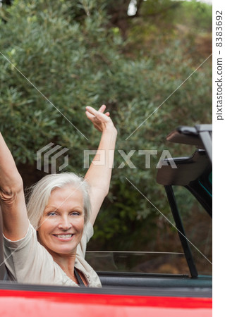 Cheerful mature woman enjoying her red convertible 8383692