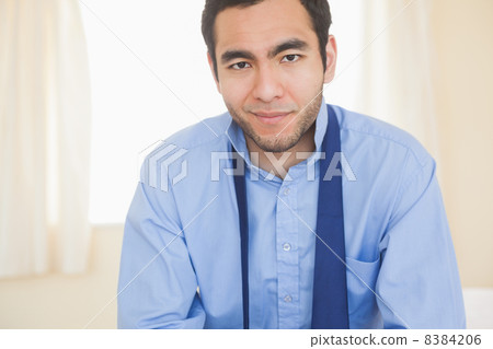 Relaxed man smiling at camera sitting on a bed Relaxed man smiling at camera sitting on a bed 8384206