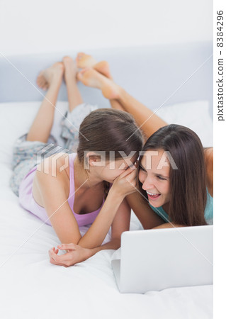 Friends lying in bed in pajamas with laptop Friends lying in bed in pajamas with laptop 8384296