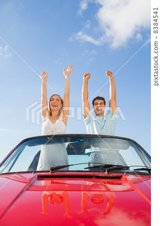 Cheerful couple standing in red cabriolet Cheerful couple standing in red cabriolet 8384541