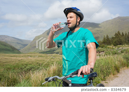 Fit man leaning on his mountain bike drinking water 8384679