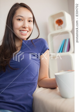 Happy young asian woman sitting on the couch holding mug Happy young asian woman sitting on the couch holding mug 8384702