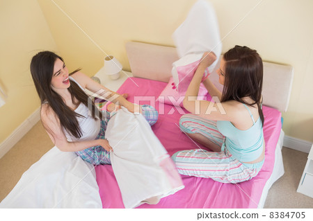 Happy friends in pajamas having a pillow fight on bed Happy friends in pajamas having a pillow fight on bed 8384705