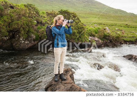 Blonde woman standing on a rock in a stream taking a photo 8384756