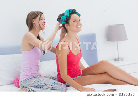 Girls sitting in bed one wearing hair rollers 8385385