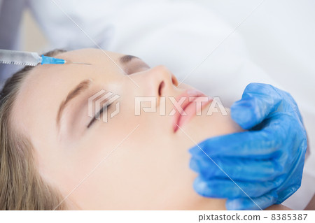 Surgeon making injection on forehead on content woman lying 8385387