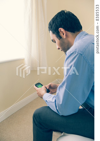 Man using a mobile phone sitting on a bed 8385533