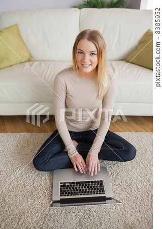 Happy woman sitting on floor using laptop Happy woman sitting on floor using laptop 8385952