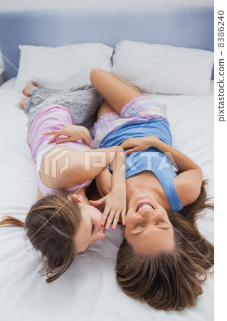 Girl whispering into her laughing friends ear Girl whispering into her laughing friends ear 8386240