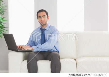 Stern businessman using his laptop while sitting on cosy sofa 8386413