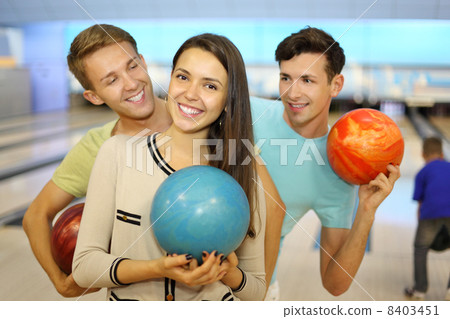 Two happy men and girl hold balls in bowling club; focus on woma 8403451