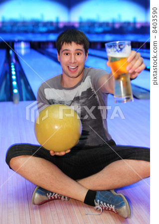 Happy young man sits on floor and holds ball and glass of beer i 8403590