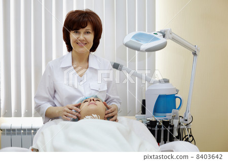 Smiling cosmetician does to the patient a facial massage in beau 8403642