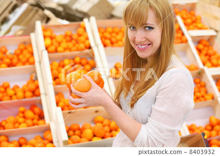 Blonde girl wearing white shirt holds oranges in store; shallow Blonde girl wearing white shirt holds oranges in store; shallow 8403932