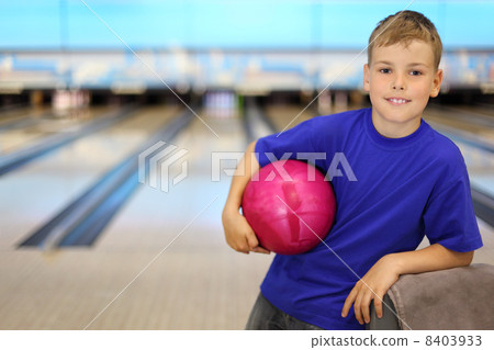 Happy boy dressed in blue T-shirt holds pink ball in bowling clu Happy boy dressed in blue T-shirt holds pink ball in bowling clu 8403933