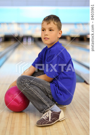 Boy dressed in blue T-shirt with pink ball sits on floor in bowl 8403961