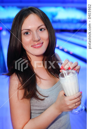 Smiling brunette woman holds milk cocktail with straw in bowling Smiling brunette woman holds milk cocktail with straw in bowling 8403982