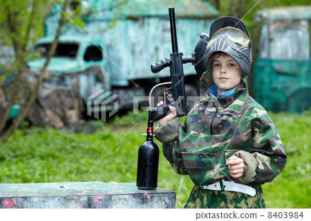 Boy in the camouflage suit holds a paintball gun barrel up, stan Boy in the camouflage suit holds a paintball gun barrel up, stan 8403984