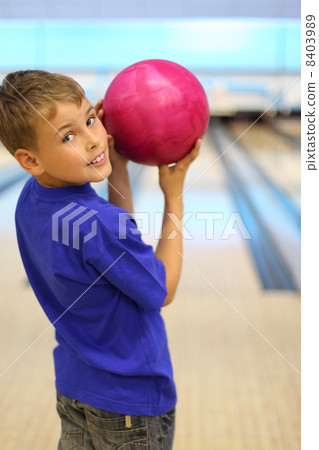 Smiling boy dressed in blue T-shirt holds pink ball in bowling c Smiling boy dressed in blue T-shirt holds pink ball in bowling c 8403989