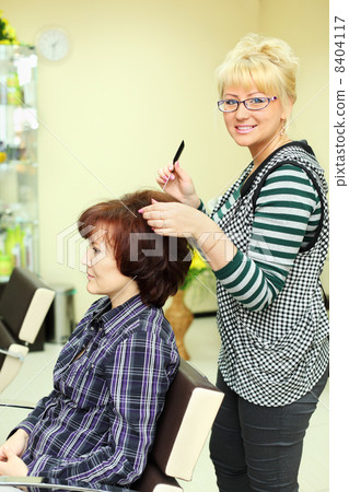 Hairdresser makes hair styling for woman by rake-comb and looks 8404117