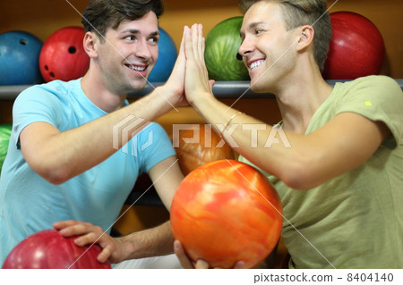 Two happy men sit near shelves with balls and touch hands in bow Two happy men sit near shelves with balls and touch hands in bow 8404140