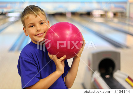 Smiling boy dressed in blue T-shirt holds pink ball in bowling c Smiling boy dressed in blue T-shirt holds pink ball in bowling c 8404144