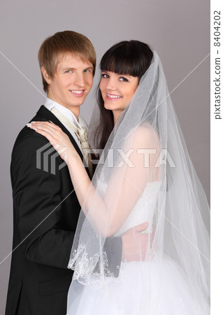 Happy young groom and bride embrace in studio on gray background 8404202