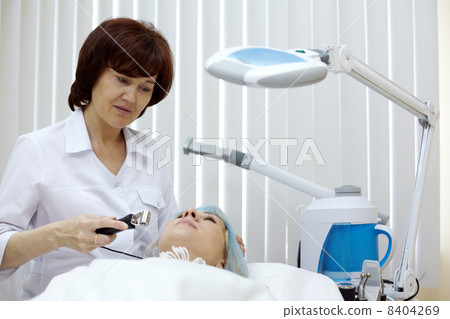 Beautician at beauty salon processes face skin of the patient wi Beautician at beauty salon processes face skin of the patient wi 8404269