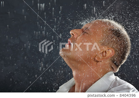 Tanned man wearing white wet shirt stands in rain and drops fall 8404396