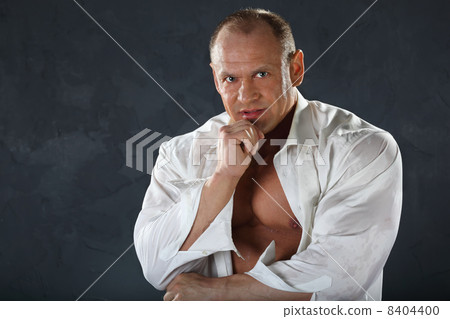 Tanned bodybuilder wearing white wet shirt looks thoughtfully at 8404400